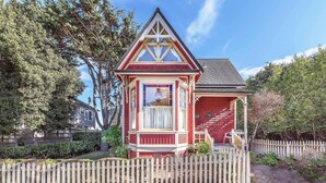 A red and white Victorian-style house with a bay window, surrounded by a picket fence and trees. - 3812 Little House - Historic Home, Walk to the Bay (Pacific Grove)