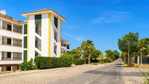 A multi-story residential building with balconies, a cobblestone street, and lush greenery. - Vila Sol: Nice apartment with large south-facing terrace and view of own park (Quarteira)
