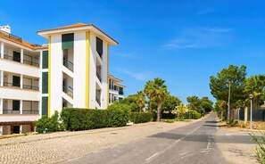 A multi-story residential building with balconies, a cobblestone street, and lush greenery. - Vila Sol: Nice apartment with large south-facing terrace and view of own park (Quarteira)