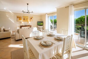 Un coin repas avec une table dressée pour quatre personnes, un canapé et un téléviseur.