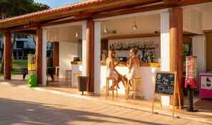 Zona de bar al aire libre con una pérgola de madera, una barra y un menú en una pizarra.
