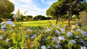 A golf course with trees and white flowers in the foreground. - Vila Sol: Nice apartment with large south-facing terrace and view of own park (Quarteira)