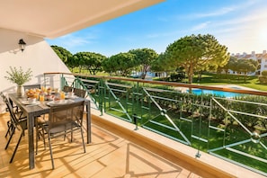 Un balcón con mesa dispuesta para el desayuno, con vistas a una piscina y un jardín cuidado.