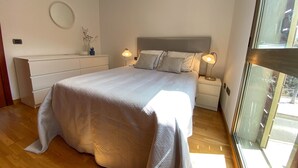 Ein Schlafzimmer mit einem großen Bett, Nachttischlampen, einem Schminktisch und einem Spiegel sowie einem Fenster.