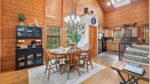 A wooden cabin interior with a dining area, kitchen, and staircase.