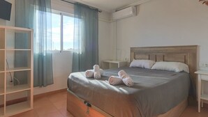 A hotel room with a large bed, a TV mounted on the wall, a wardrobe, and a window with curtains. - 032 - Parque y Playa 001 - comfortHOLIDAYS (Santa Pola)