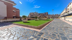 A courtyard with a paved walkway, a small lawn area, and a building with balconies. - 032 - Parque y Playa 001 - comfortHOLIDAYS (Santa Pola)