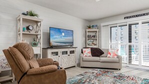 A living room with a brown recliner, a beige sofa, a TV on a wooden cabinet, and a colorful rug. - Fully remodeled 2 bedroom condo on the ocean block in North OC (Ocean City)