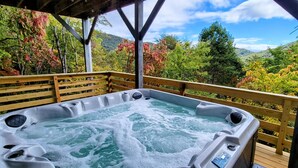 Ein Whirlpool auf einer Holzterrasse mit Blick auf einen bewaldeten Hang.