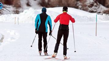Dos personas esquiando por un sendero nevado, usando bastones de esquí, con chaquetas y cascos.