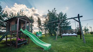 A playground with a wooden playhouse, a green slide, a swing set, and a bench. - Apartament Na Wierchu (Poronin)