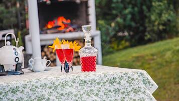 A table with a floral tablecloth, a teapot, two glasses with a red drink, and a decanter with a red liquid.