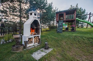 Un entorno rústico al aire libre con una chimenea de piedra, una casita de juegos de madera y un tobogán.