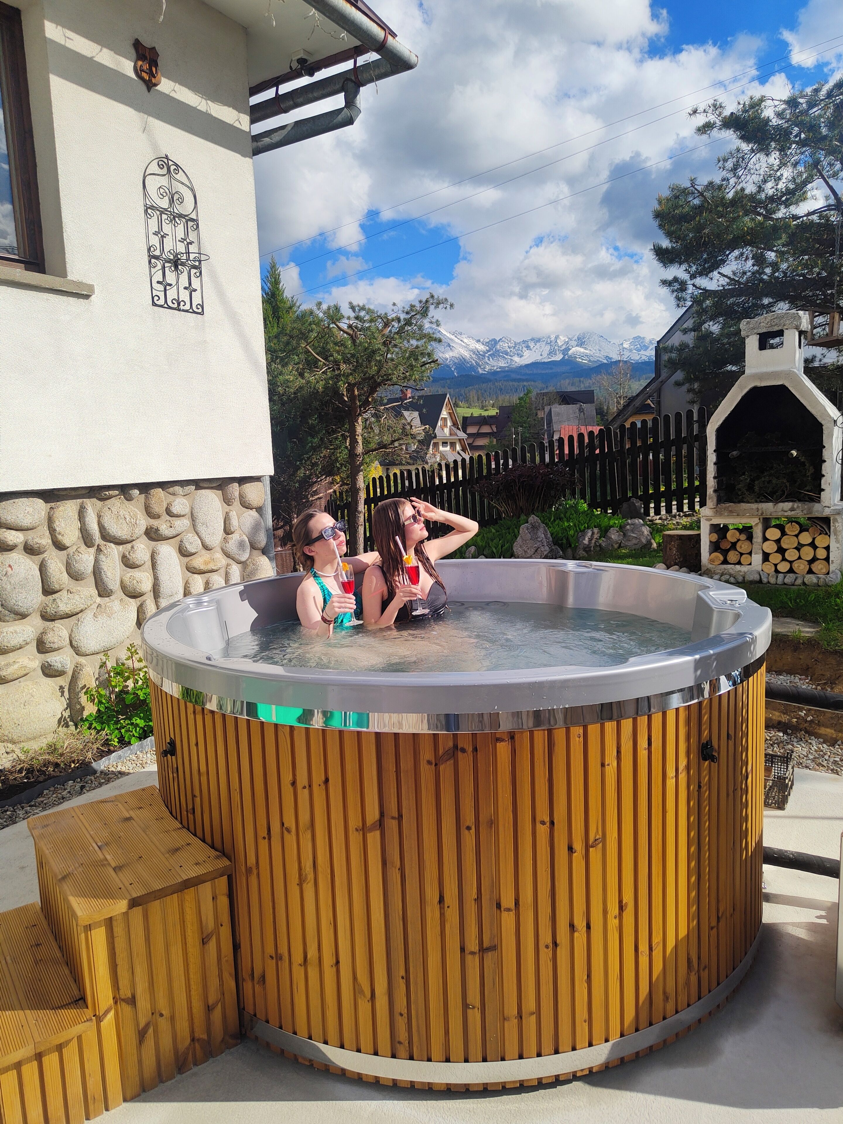 A hot tub with two people in it, surrounded by a stone wall and wooden deck.