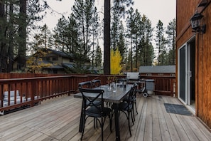 A wooden deck with a table and chairs, surrounded by a wooden fence, and overlooking a forested area.