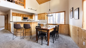 A spacious kitchen with a wooden ceiling, a dining area with a large table and chairs, and a view of the outdoors through a window.