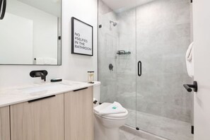 A modern bathroom with a glass shower enclosure, a white toilet, and a sink with a mirror above it. - Luxury 3BR/2BA Creekside: Hot tub, A/C, Secure Bike Storage, Mountain Views (Whistler)