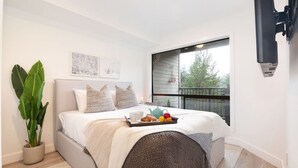 A bedroom with a bed, a potted plant, a tray with breakfast items, and a window with a view of greenery. - Luxury 3BR/2BA Creekside: Hot tub, A/C, Secure Bike Storage, Mountain Views (Whistler)