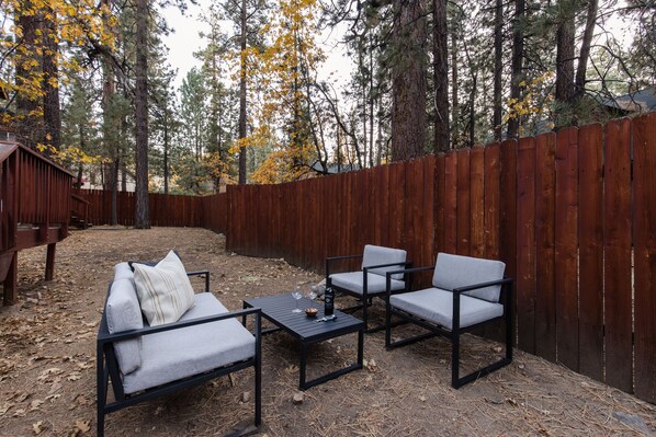 An outdoor seating area with a wooden fence, a sofa, two chairs, and a table.