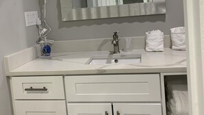 Une salle de bain avec un meuble-lavabo blanc, un miroir, un sèche-cheveux et des serviettes.