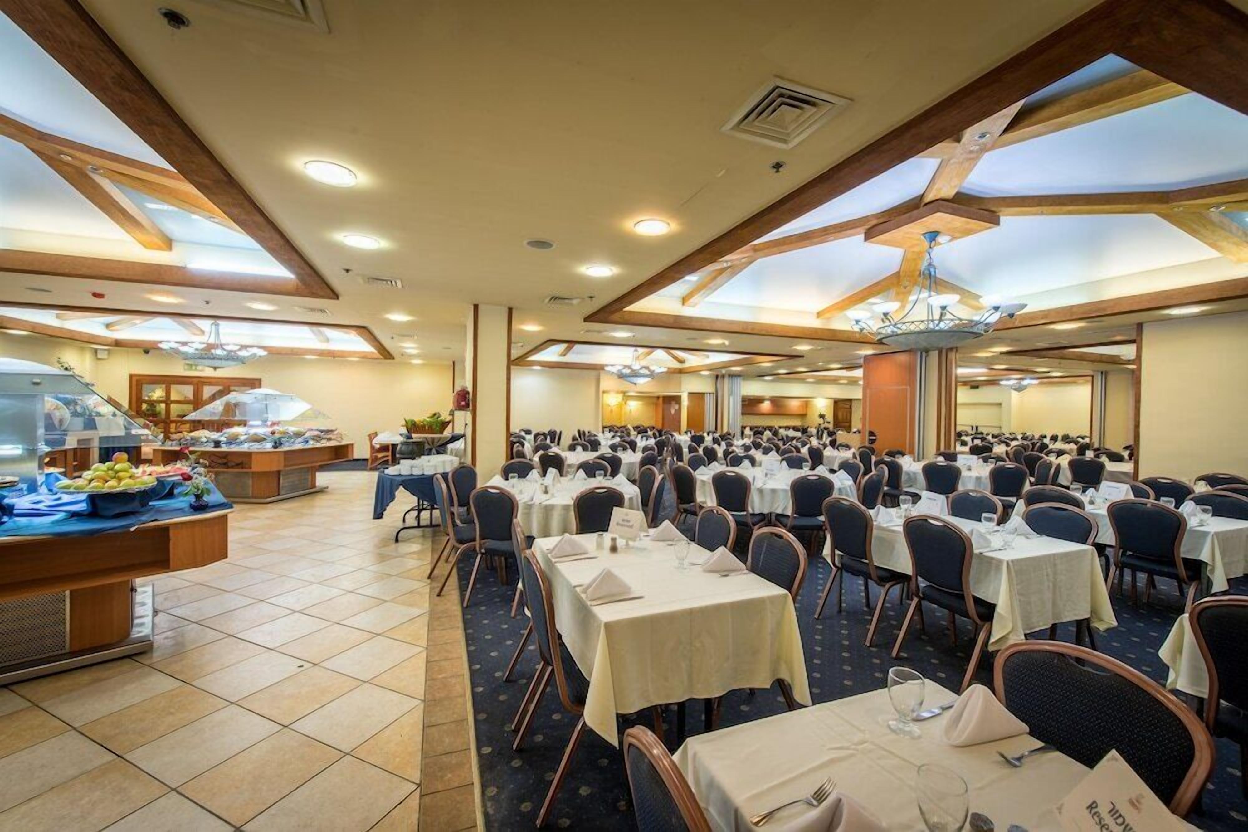 A large banquet hall with numerous round tables, a buffet area, and a high ceiling with skylights.