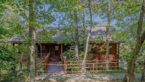 Un rustico chalet circondato da alberi, con una veranda in legno e un portico coperto.