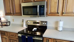 A kitchen with wooden cabinets, a stainless steel microwave, a black stove, and a countertop. - Palma Sola Pool Home Bradenton (Bradenton)