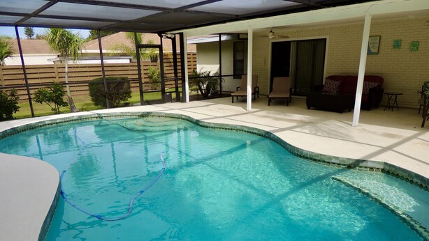 A swimming pool with a curved edge, surrounded by a covered patio area with chairs and a table. - Palma Sola Pool Home Bradenton (Bradenton)