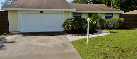 A single-story house with a white garage door, a front yard with a well-maintained lawn, and a street lamp.