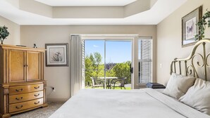 Un dormitorio con una cama grande, un aparador de madera, un cuadro enmarcado y vistas al exterior a través de un ventanal corredero.