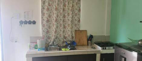 A kitchen with a sink, a stove, and a coffee maker. There is a cutting board and a basket of utensils on the counter.