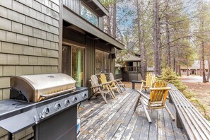 Eine Holzterrasse mit Grill, Gartenmöbeln und Blick auf die umliegenden Bäume.