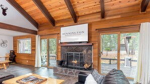 Een gezellig cabin interieur met een stenen openhaard, een leren bank en een bordje met de tekst 'BENNINGTON SUNRIVER VACATIONS'.