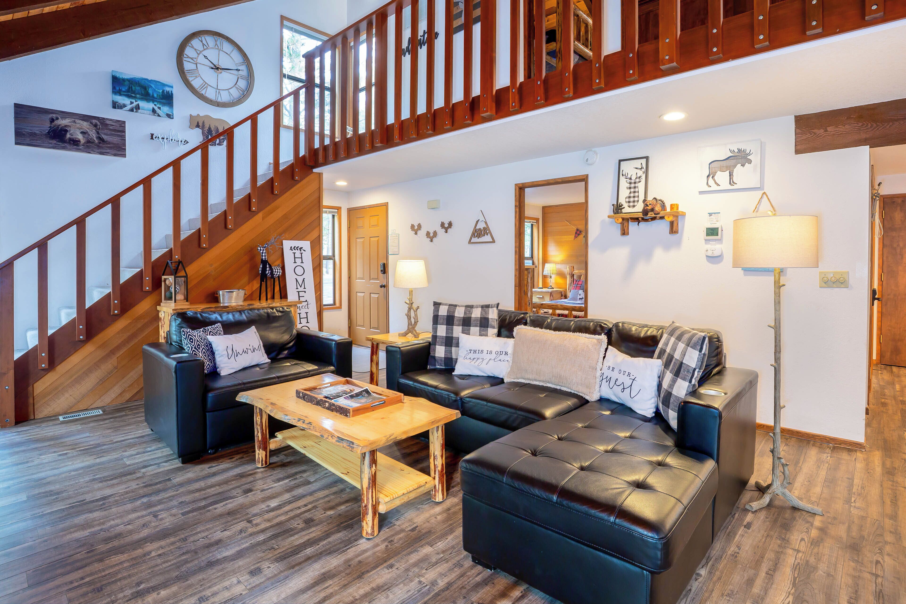 A spacious living area with a staircase, leather sofas, a wooden coffee table, and various wall decorations including a clock and framed pictures.