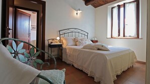 Een slaapkamer met een bed, nachtkastje, lamp, stoel en raam.