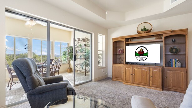 A spacious living room with a large glass door leading to a patio, a comfortable sofa, a television, and wooden cabinets.