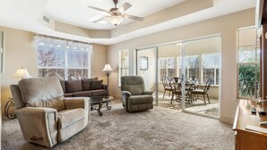 A spacious living room with a ceiling fan, a sofa, a recliner, and a dining area with chairs and a table.