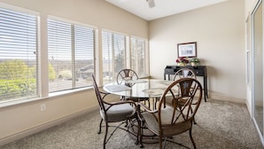 A dining area with a round table and four chairs, large windows with blinds, a ceiling fan, and a small table with a vase of flowers. - 1 Bedroom Walk-in Golf Condo feat. Sunroom with a Beautiful Property View (Branson)