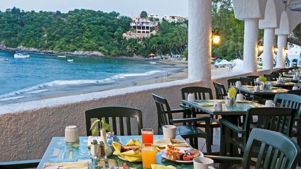 An outdoor dining area with tables set for breakfast overlooking a beach and ocean. - Tesoro Manzanillo (Manzanillo)