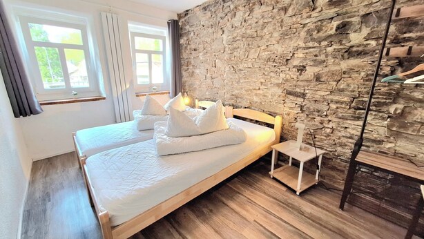 Cama doble con ropa de cama y almohadas blancas, pared de piedra y suelo de madera en una habitación de hotel.