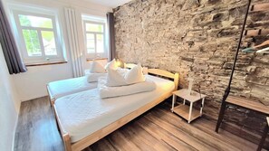Cama doble con ropa de cama y almohadas blancas, pared de piedra y suelo de madera en una habitación de hotel.