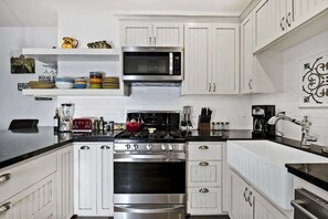 Una cocina moderna con armarios blancos, una estufa de acero inoxidable, un microondas y un hervidor rojo.
