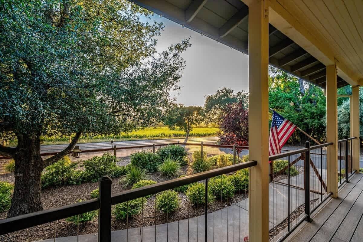 A covered outdoor area with a view of a road, a flag, and a tree.