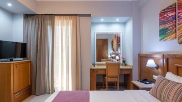Habitación de hotel con cama, escritorio, silla, televisor, lámpara de escritorio y un espejo grande.