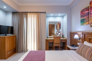 Habitación de hotel con cama, escritorio, silla, televisor, lámpara de escritorio y un espejo grande.