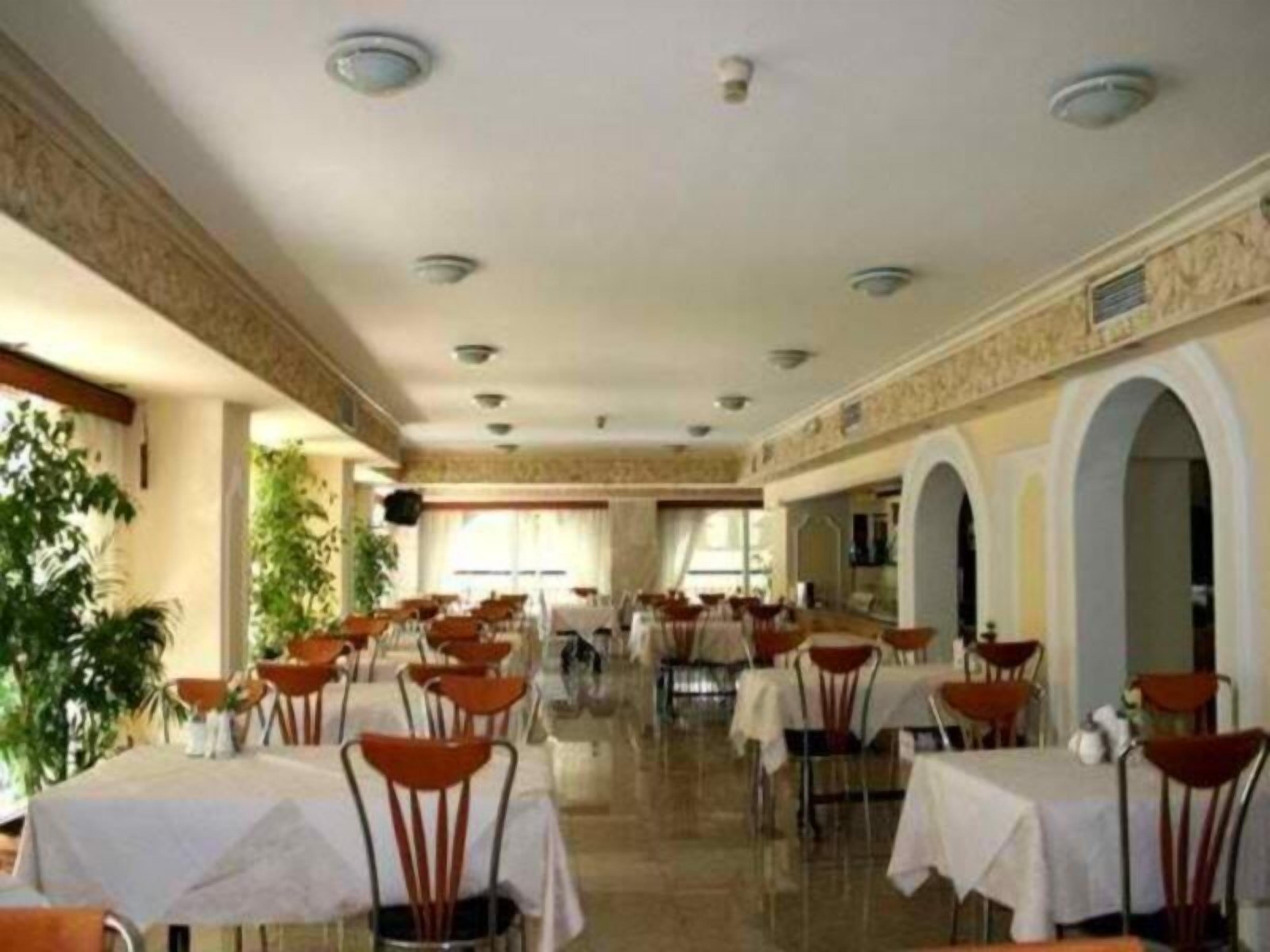 Un amplio comedor interior con varias mesas y sillas, un techo alto con iluminación empotrada y vistas al exterior a través de grandes ventanales.
