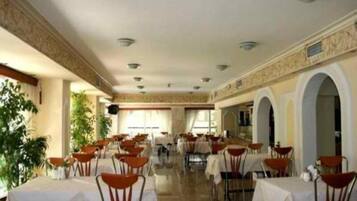 Un amplio comedor interior con varias mesas y sillas, un techo alto con iluminación empotrada y vistas al exterior a través de grandes ventanales.