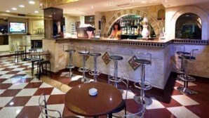 Un espace bar avec un sol à carreaux, des tabourets de bar et un comptoir où travaille un barman.