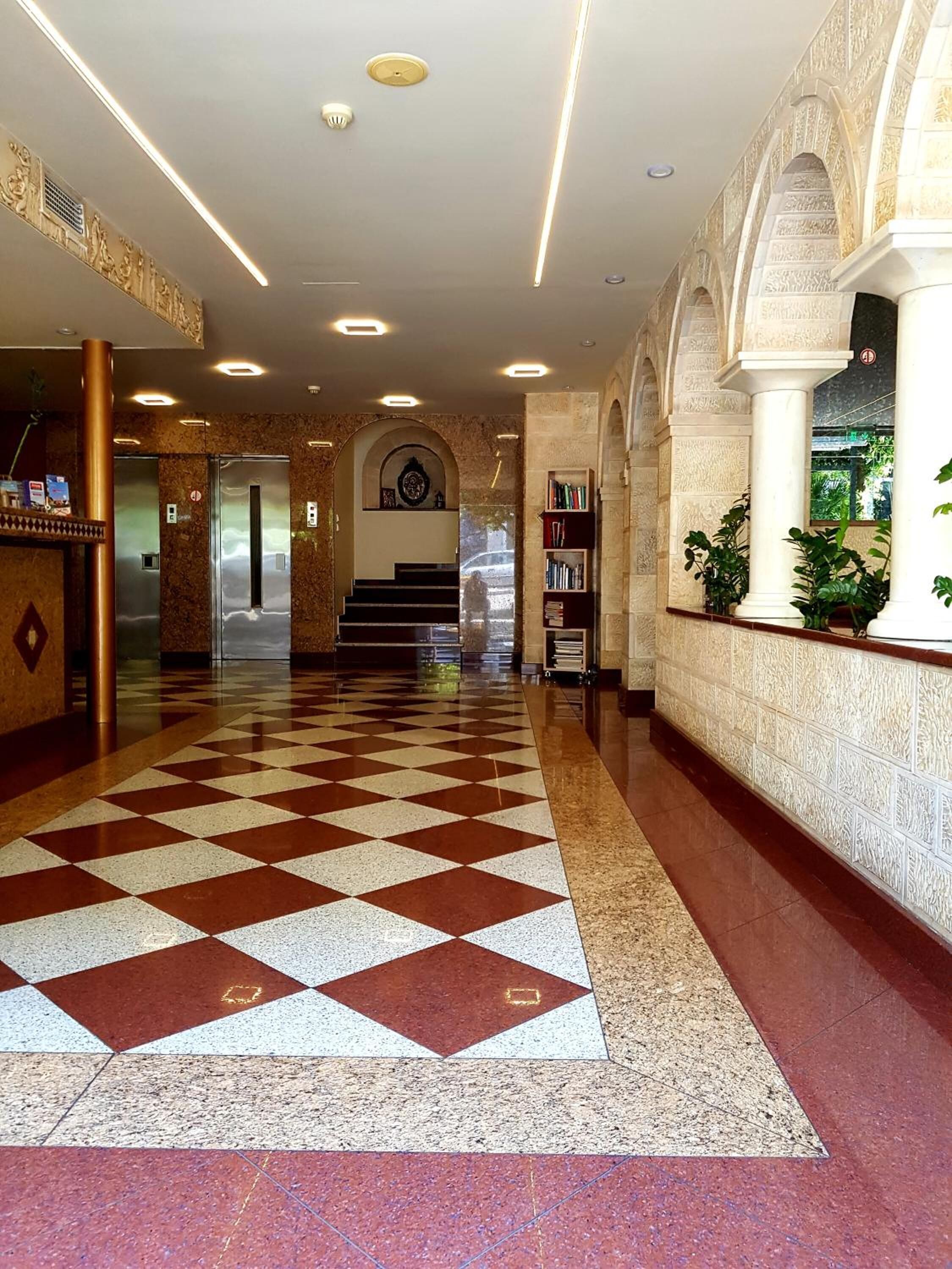 Un vestíbulo de hotel con piso a cuadros, una recepción, una escalera y una estantería.