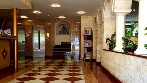 Un hall d’hôtel avec un sol à carreaux, un comptoir d’accueil, un escalier et une bibliothèque.